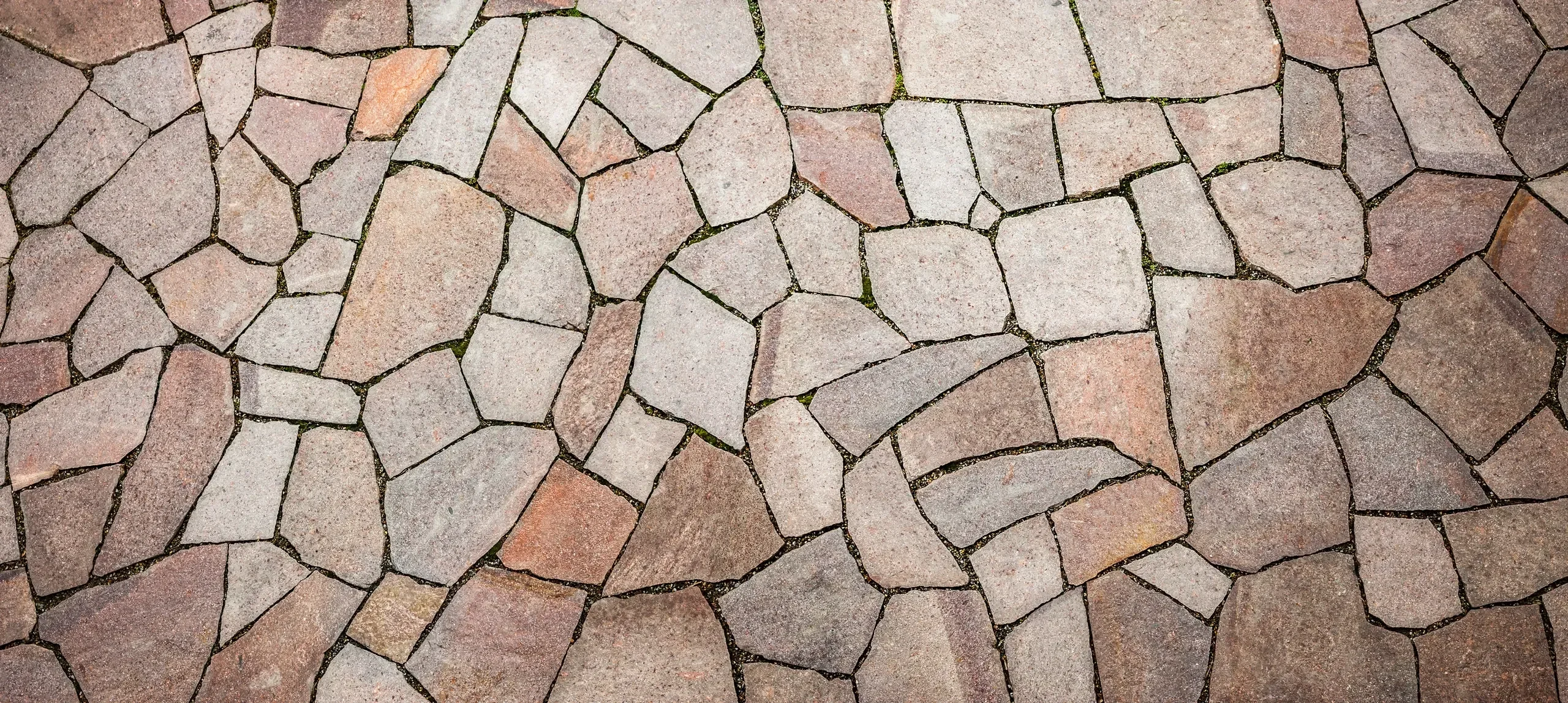 A detailed view of a completed crazy paving surface composed of irregularly shaped flagstones in varied shades of pink, gray, and brown.