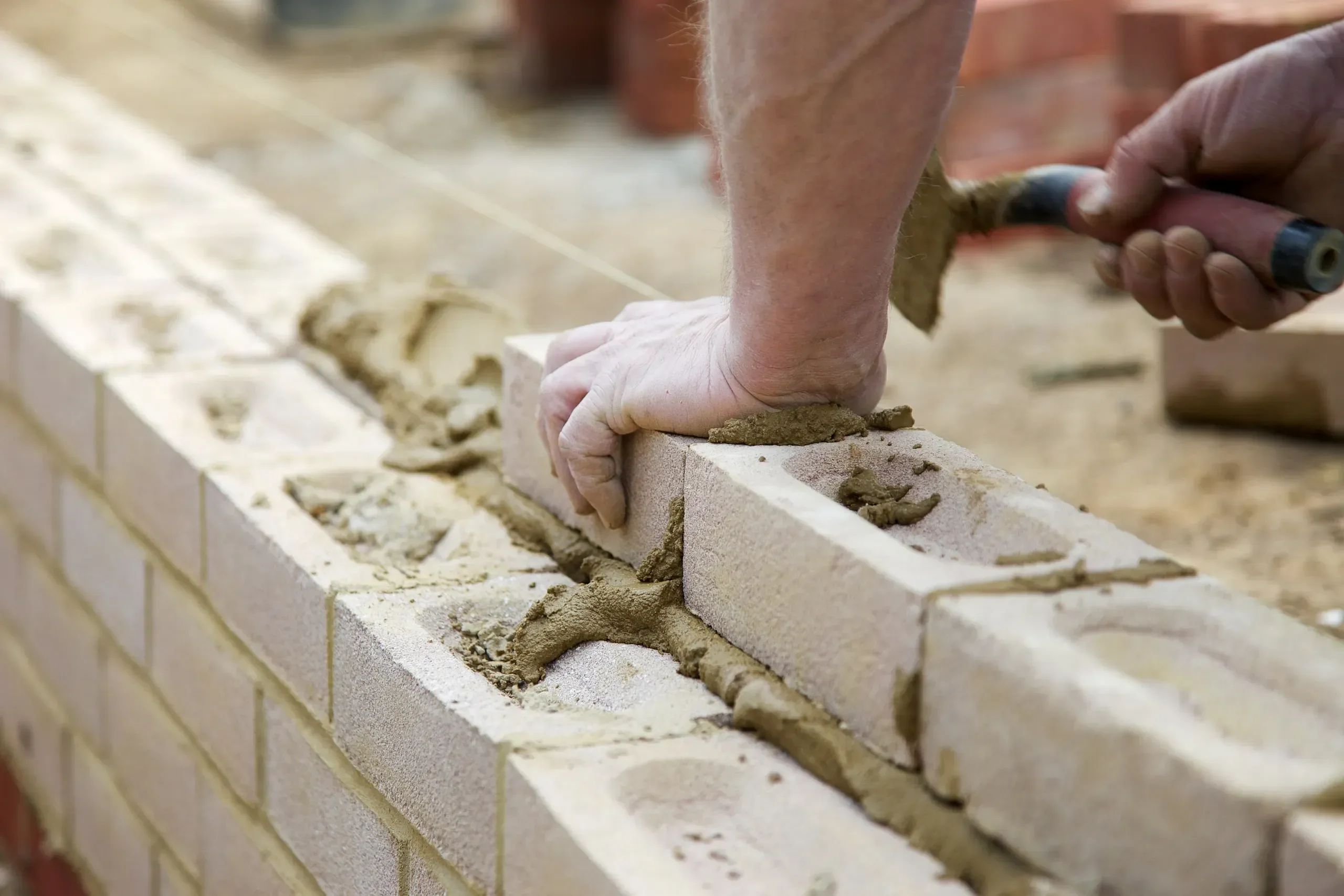 A mason beds a concrete block in fresh mortar while rebuilding a wall.