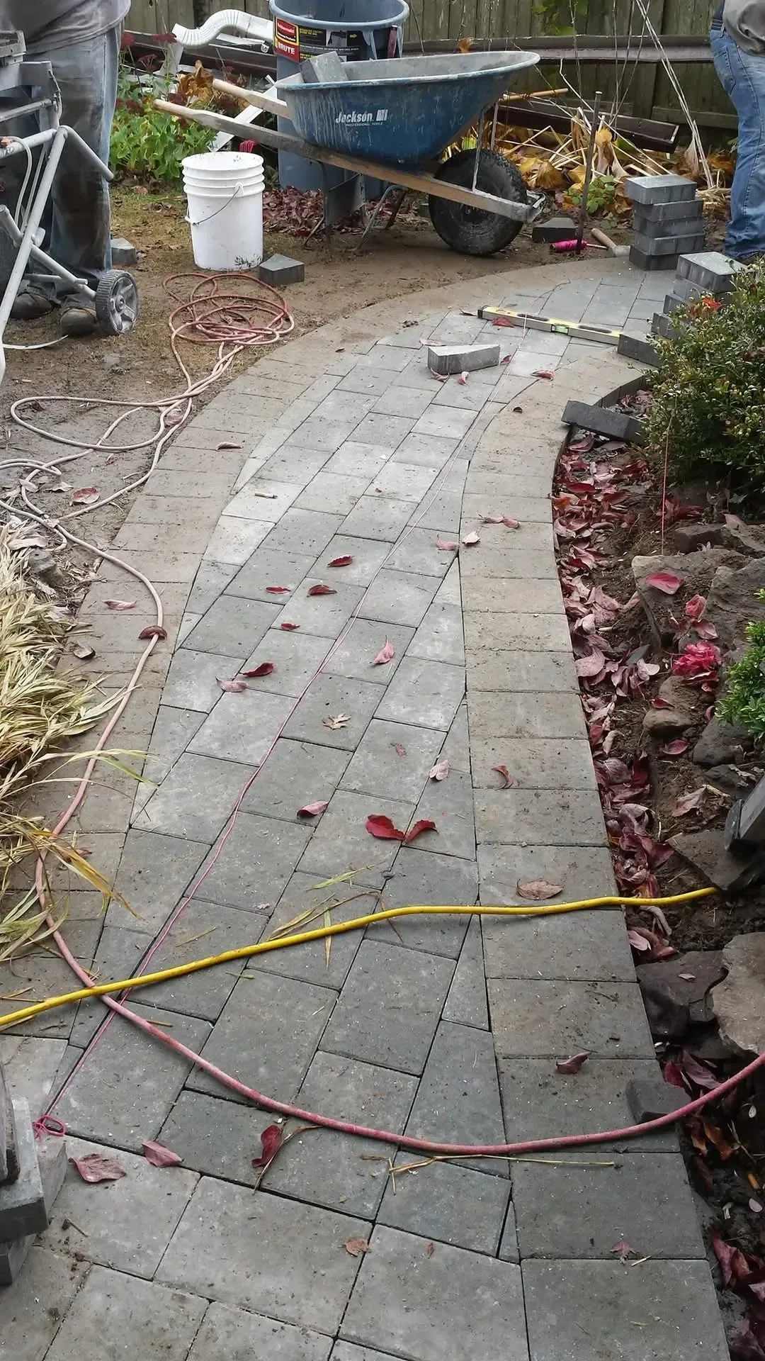 Teams install a curved paver walkway surrounded by tools and materials.