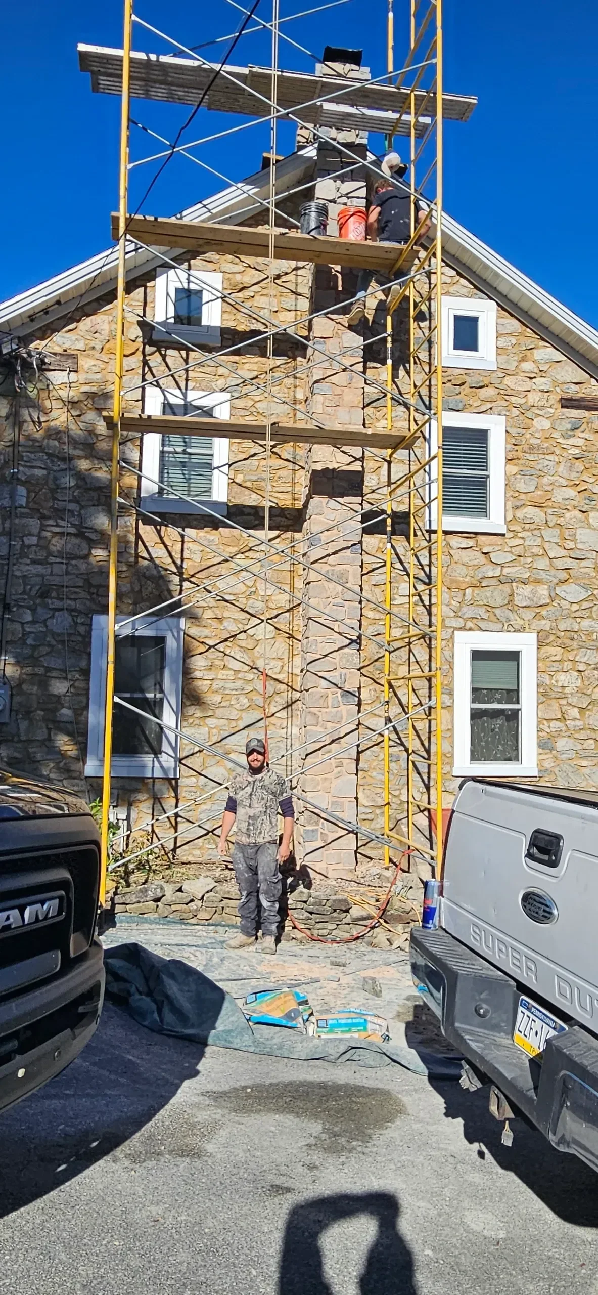 Technicians restore a stone chimney from elevated scaffolding.
