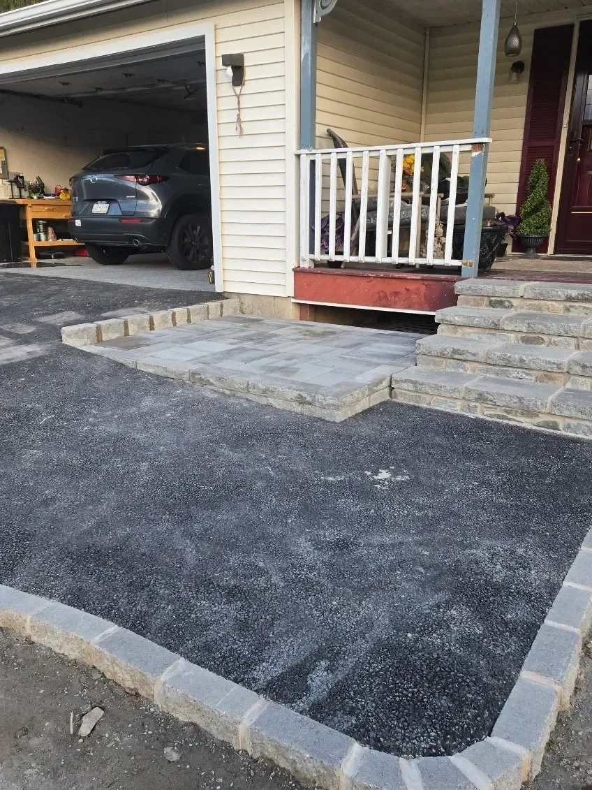 Newly installed stone curbing borders a dark gravel area leading to a gray paver landing and natural stone steps at a residential entrance.